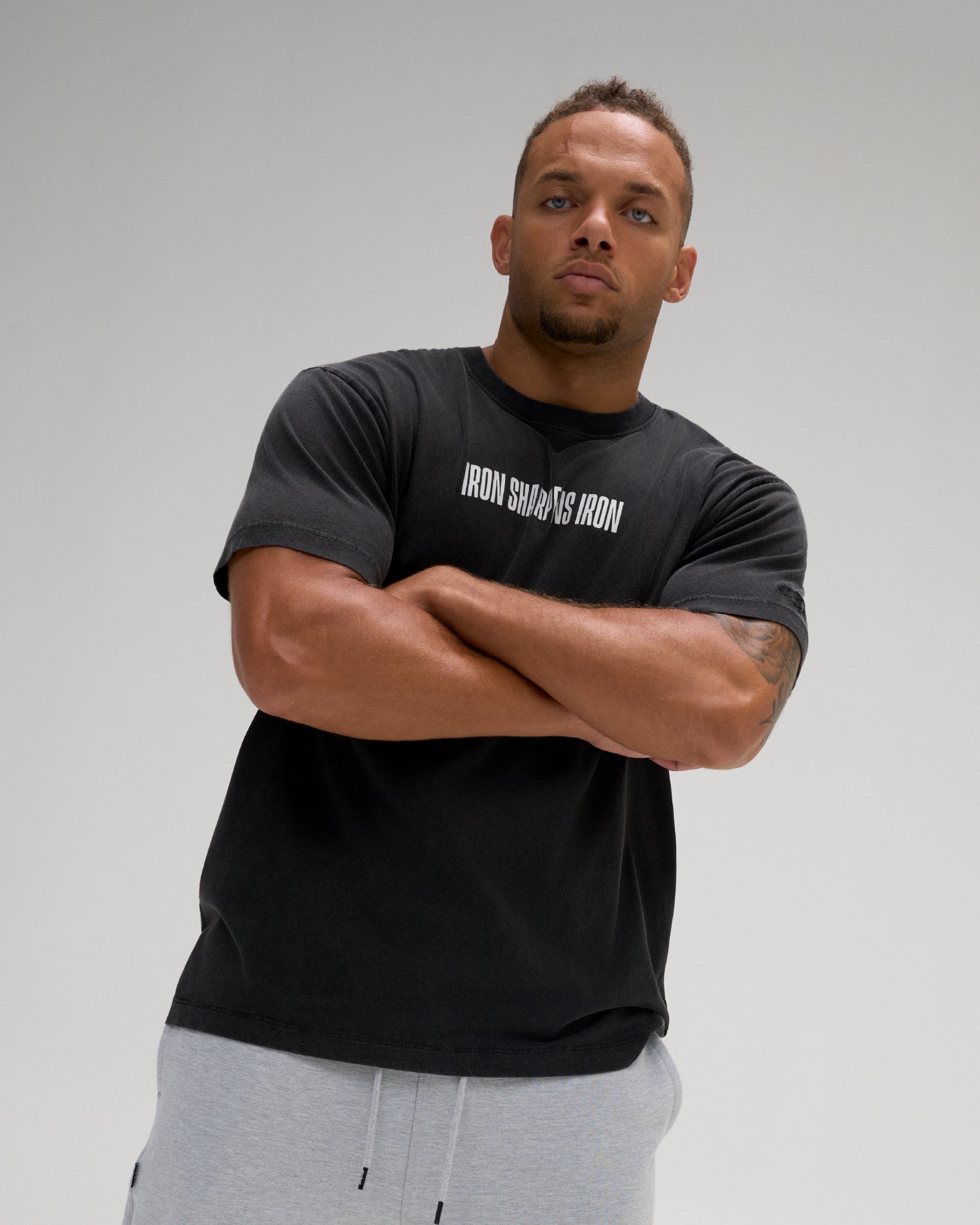 Front view of a model wearing the RUDIS Iron Sharpens Iron Classic Cotton T-Shirt in Washed Black, highlighting the white chest lettering, crew neckline and relaxed silhouette.