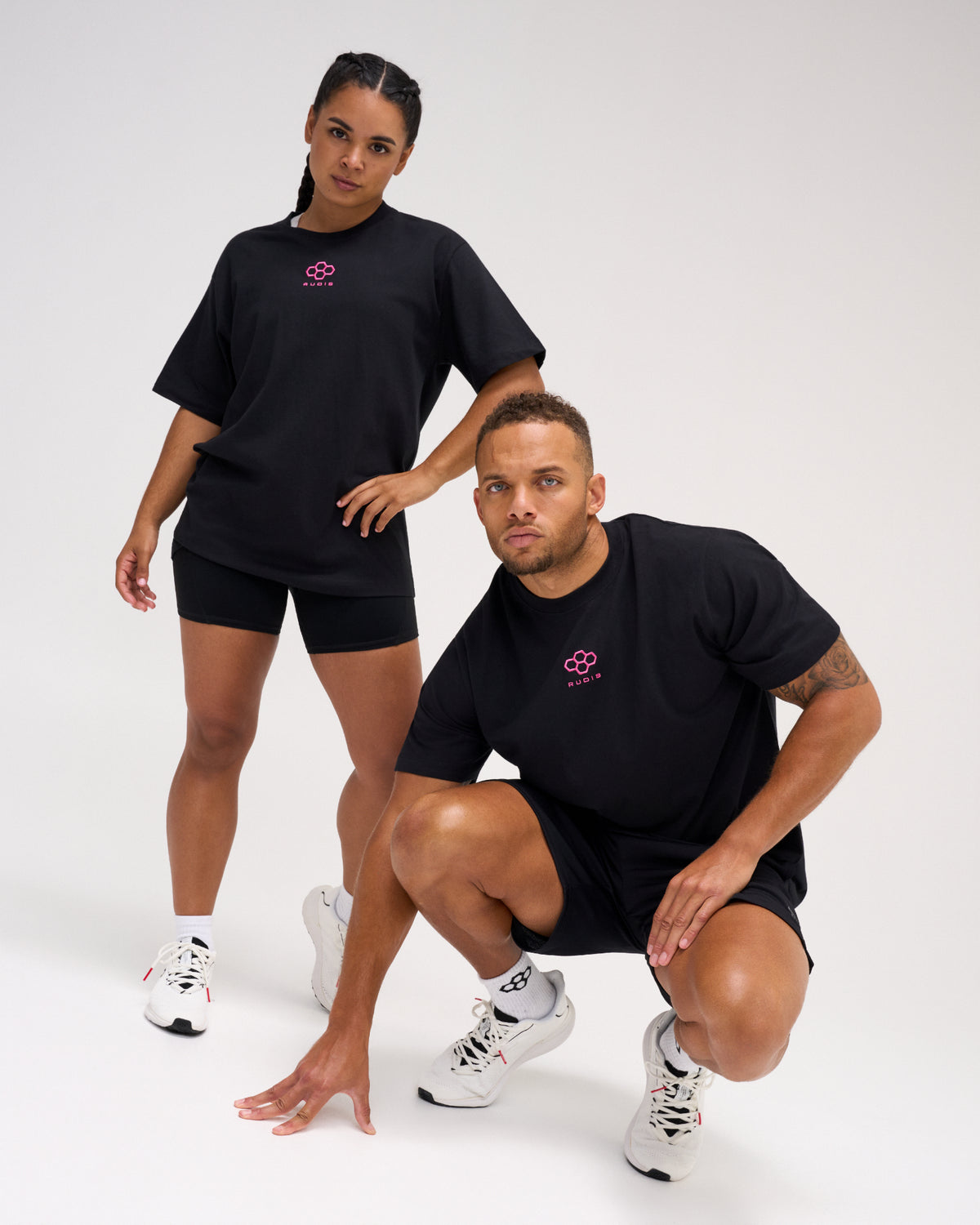 Two models wearing the RUDIS Hex Classic Cotton T-Shirt in Black/Pink, featuring bright pink embroidered Hex logos and relaxed short-sleeve silhouettes.