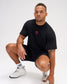 Male model crouching in the RUDIS Hex Classic Cotton T-Shirt in Black/Pink, showcasing the pink Hex chest embroidery and classic crewneck fit.