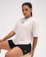 Female model seated in the RUDIS Hex Classic Cotton T-Shirt in Bone, highlighting the black embroidered Hex logo, crew neckline and relaxed fit.
