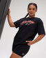 Female model wearing the RUDIS Script Wrestling Classic Cotton T-Shirt in Black with a bold coral Wrestling graphic, green Hex logo and relaxed fit.