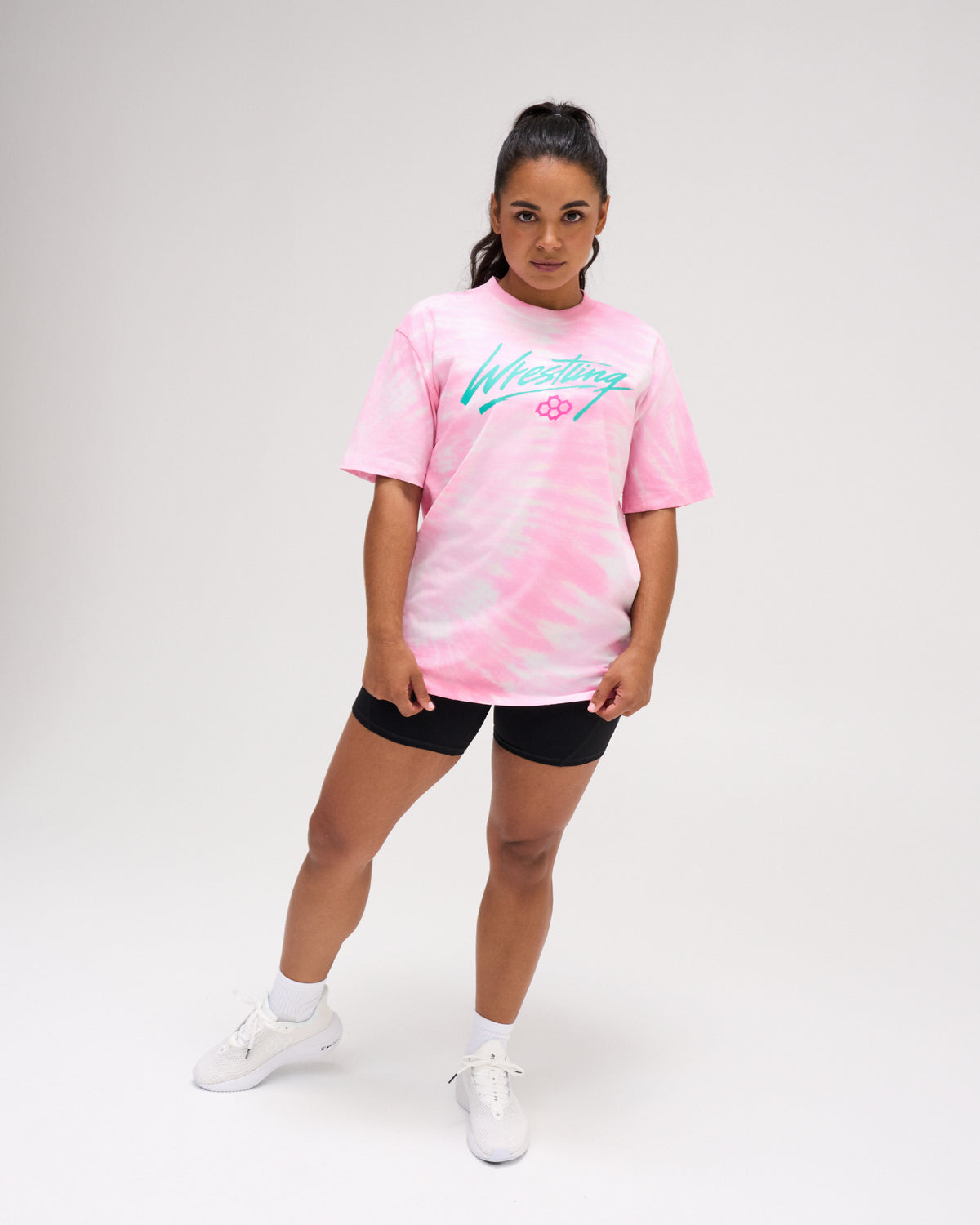 Female model standing in the RUDIS Script Wrestling Classic Cotton T-Shirt in Tie-Dye Pink, showcasing the teal Wrestling graphic and relaxed silhouette.