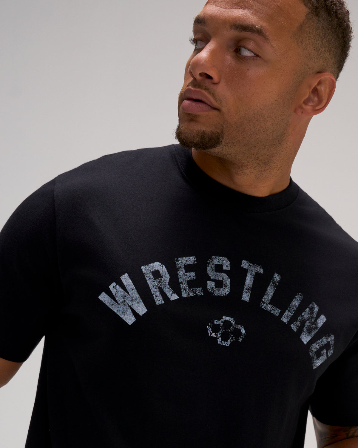 Close-up of the RUDIS Wrestling Classic Cotton T-Shirt in Black, highlighting distressed gray Wrestling lettering and the RUDIS Hex logo.