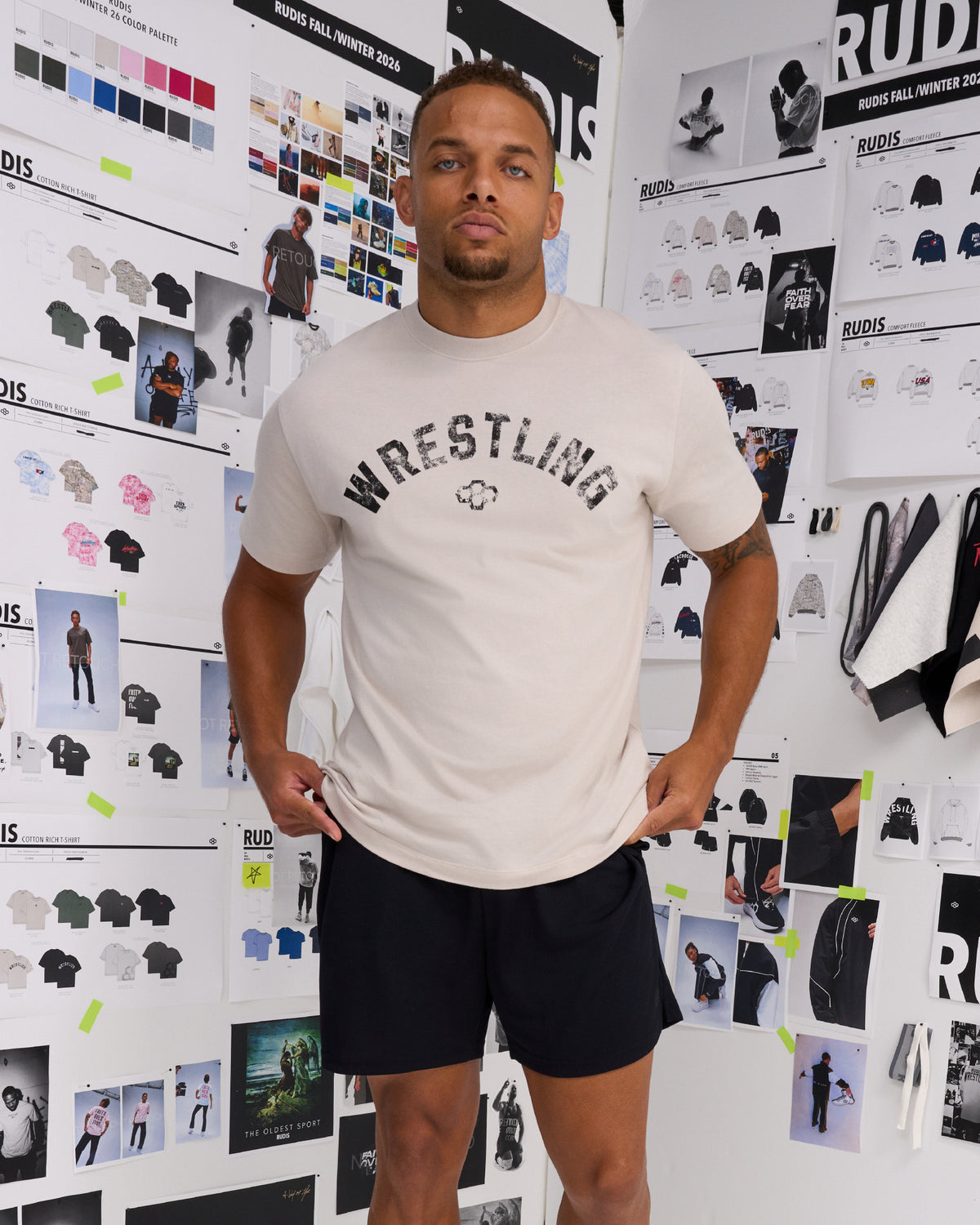 Male model standing in the RUDIS Wrestling Classic Cotton T-Shirt in Bone, showcasing the vintage-inspired Wrestling chest graphic and RUDIS Hex logo.