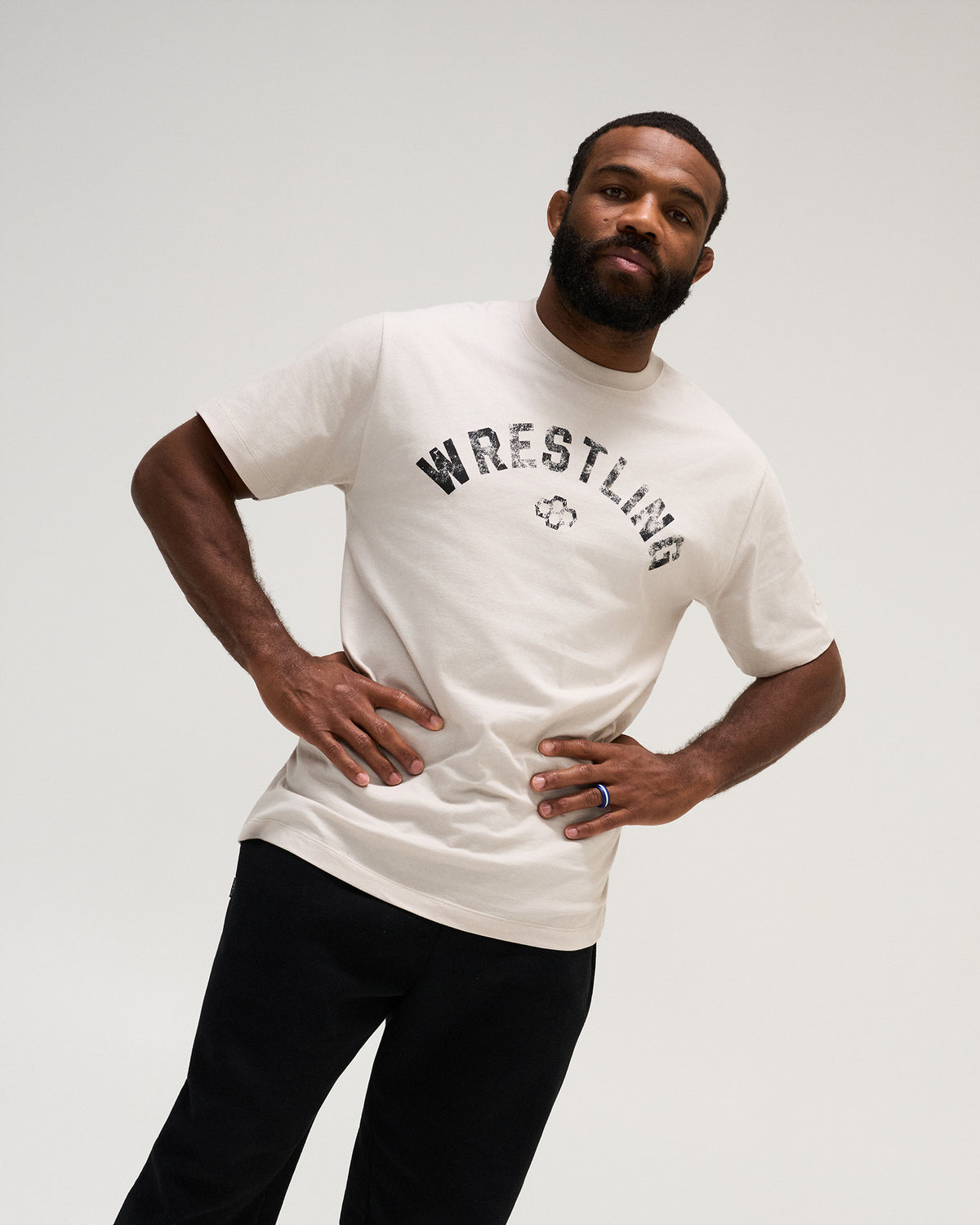 Male model wearing the RUDIS Wrestling Classic Cotton T-Shirt in Bone with a distressed black arched Wrestling graphic and relaxed fit.