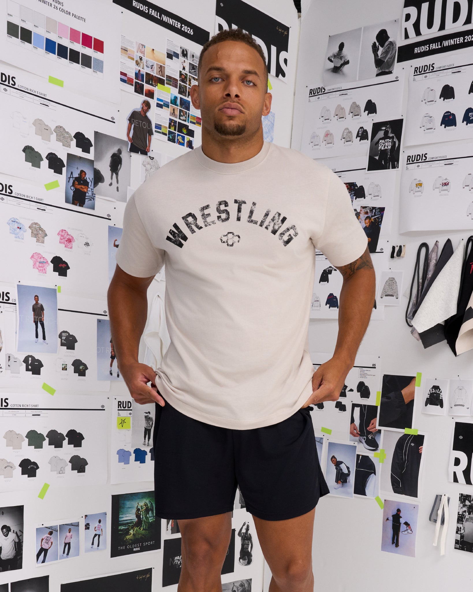 Male model standing in the RUDIS Wrestling Classic Cotton T-Shirt in Bone, showcasing the vintage-inspired Wrestling chest graphic and RUDIS Hex logo.