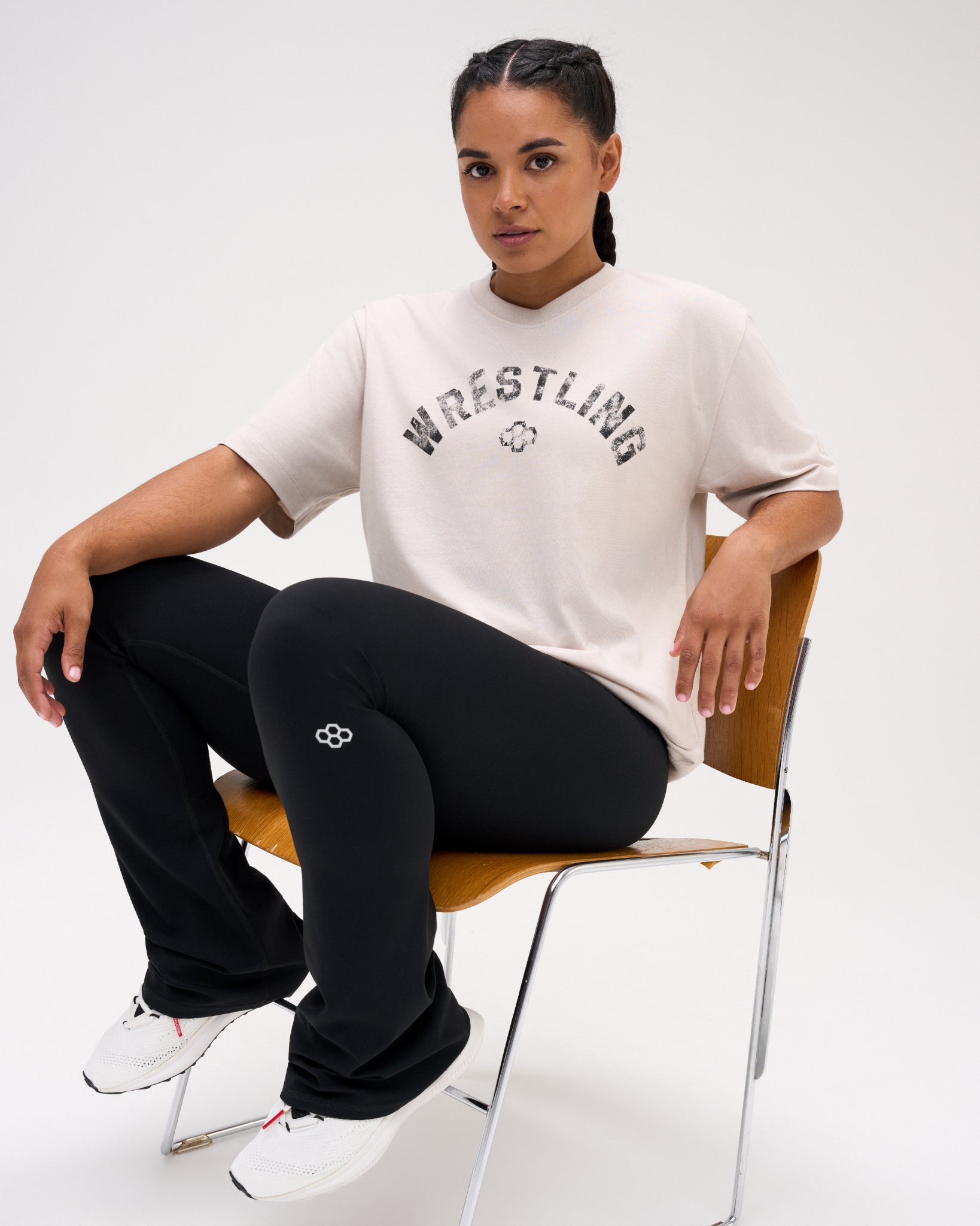 Female model seated in the RUDIS Wrestling Classic Cotton T-Shirt in Bone, styled with black pants and featuring distressed Wrestling lettering.