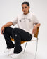 Female model seated in the RUDIS Wrestling Classic Cotton T-Shirt in Bone, styled with black pants and featuring distressed Wrestling lettering.