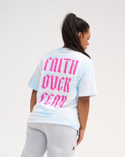 Female model wearing the RUDIS Faith Over Fear Classic Cotton T-Shirt in Blue Tie Dye, showing oversized pink gothic Faith Over Fear lettering on the back.