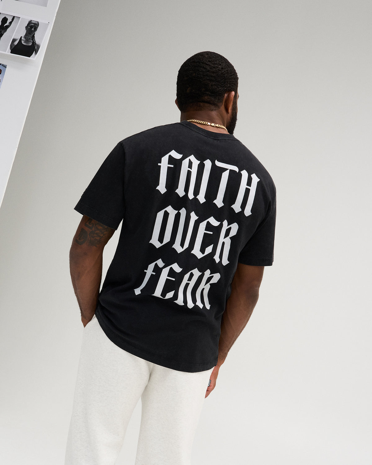 Male model wearing the RUDIS Faith Over Fear Classic Cotton T-Shirt in Washed Black, featuring large white gothic Faith Over Fear lettering across the back.
