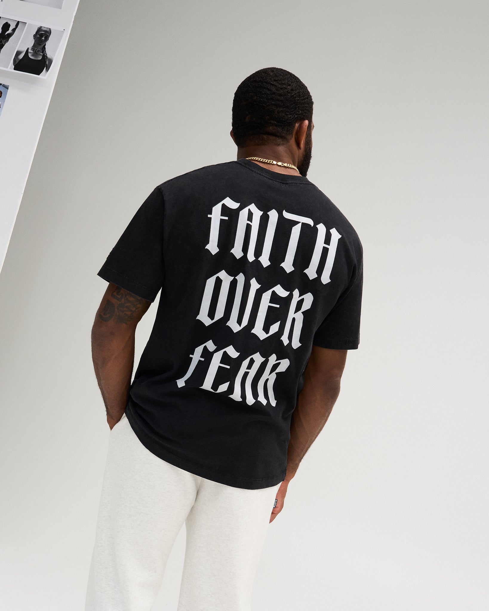 Male model wearing the RUDIS Faith Over Fear Classic Cotton T-Shirt in Washed Black, featuring large white gothic Faith Over Fear lettering across the back.
