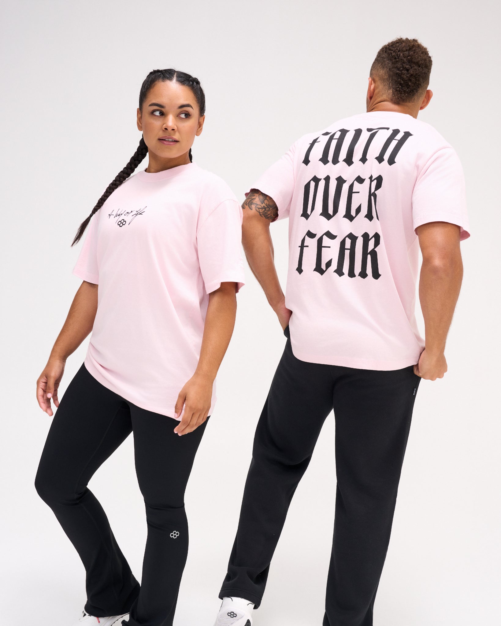 Male and female models wearing the RUDIS Faith Over Fear Classic Cotton T-Shirt in Washed Pink, displaying black chest artwork and gothic back lettering.