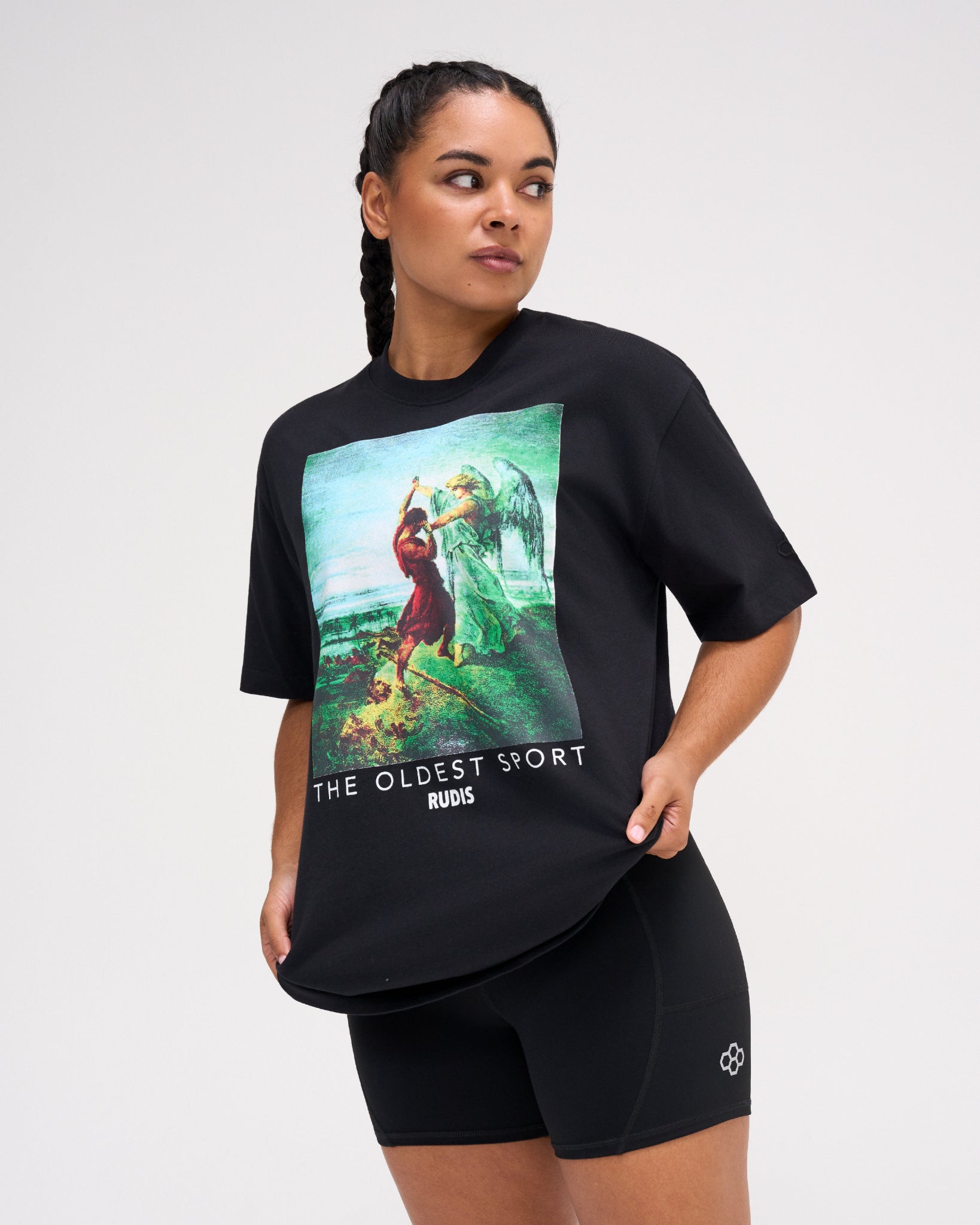 Female model wearing the RUDIS Divine Struggle Relaxed Cotton T-Shirt in Washed Black, showcasing vintage-inspired wrestling artwork, The Oldest Sport text, and a relaxed fit.