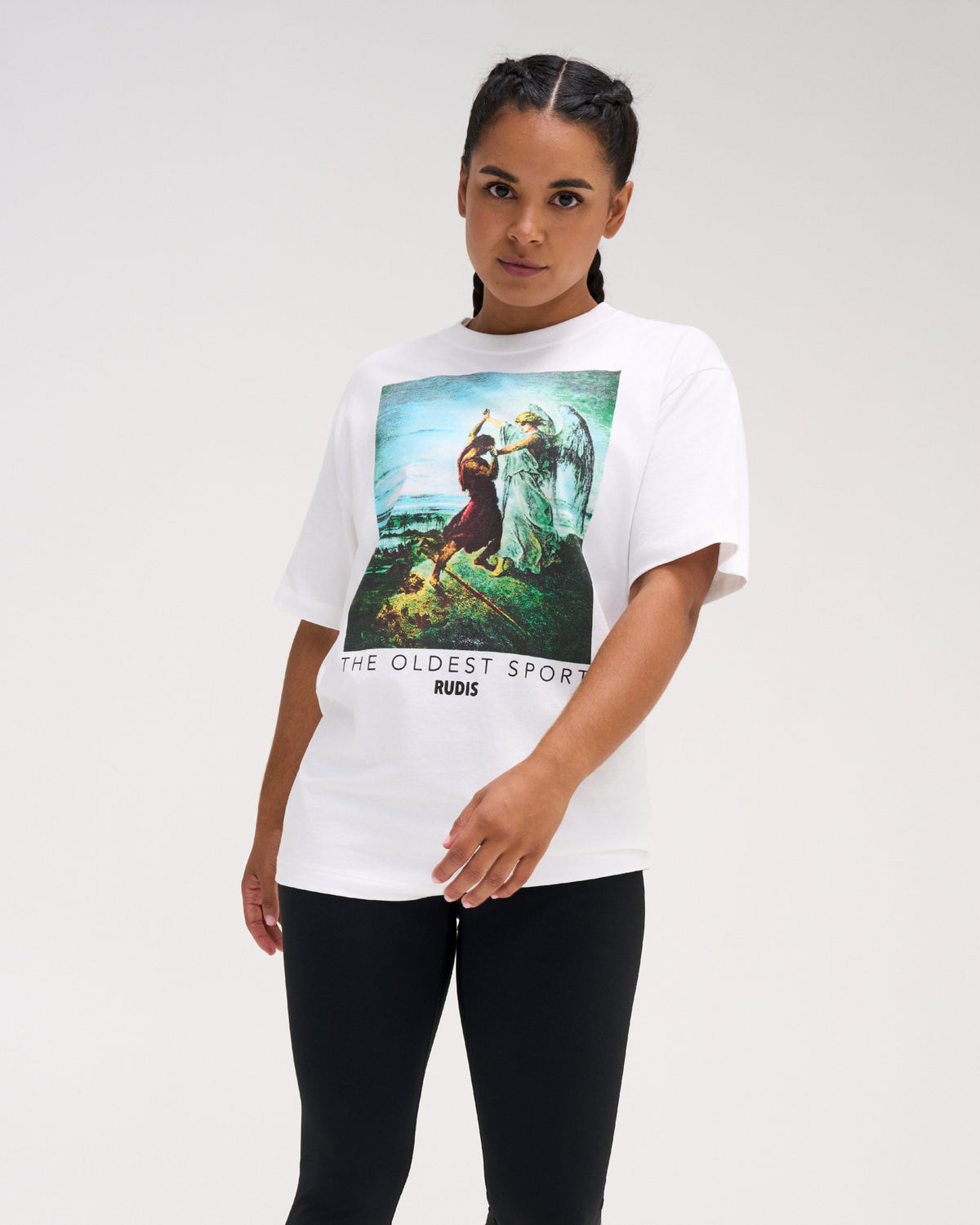 Female model wearing the RUDIS Divine Struggle Relaxed Cotton T-Shirt in White, highlighting the colorful angel and wrestler illustration, RUDIS logo, and relaxed silhouette.