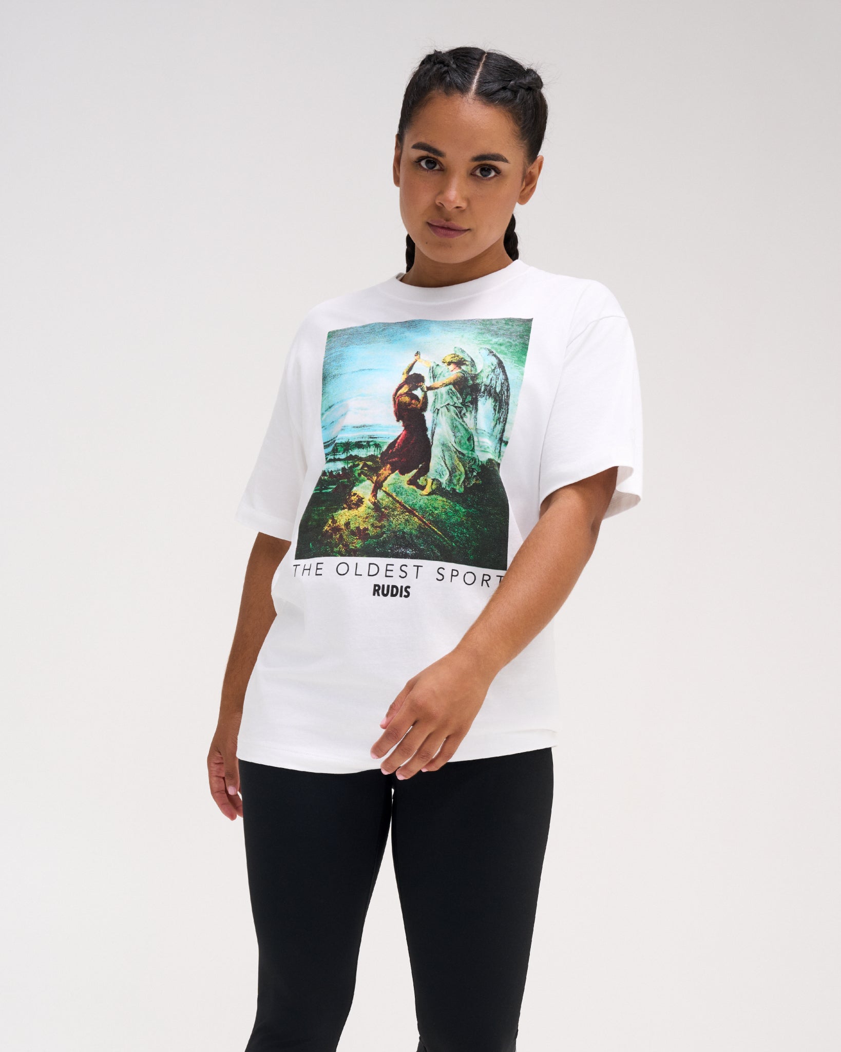 Female model wearing the RUDIS Divine Struggle Relaxed Cotton T-Shirt in White, highlighting the colorful angel and wrestler illustration, RUDIS logo, and relaxed silhouette.