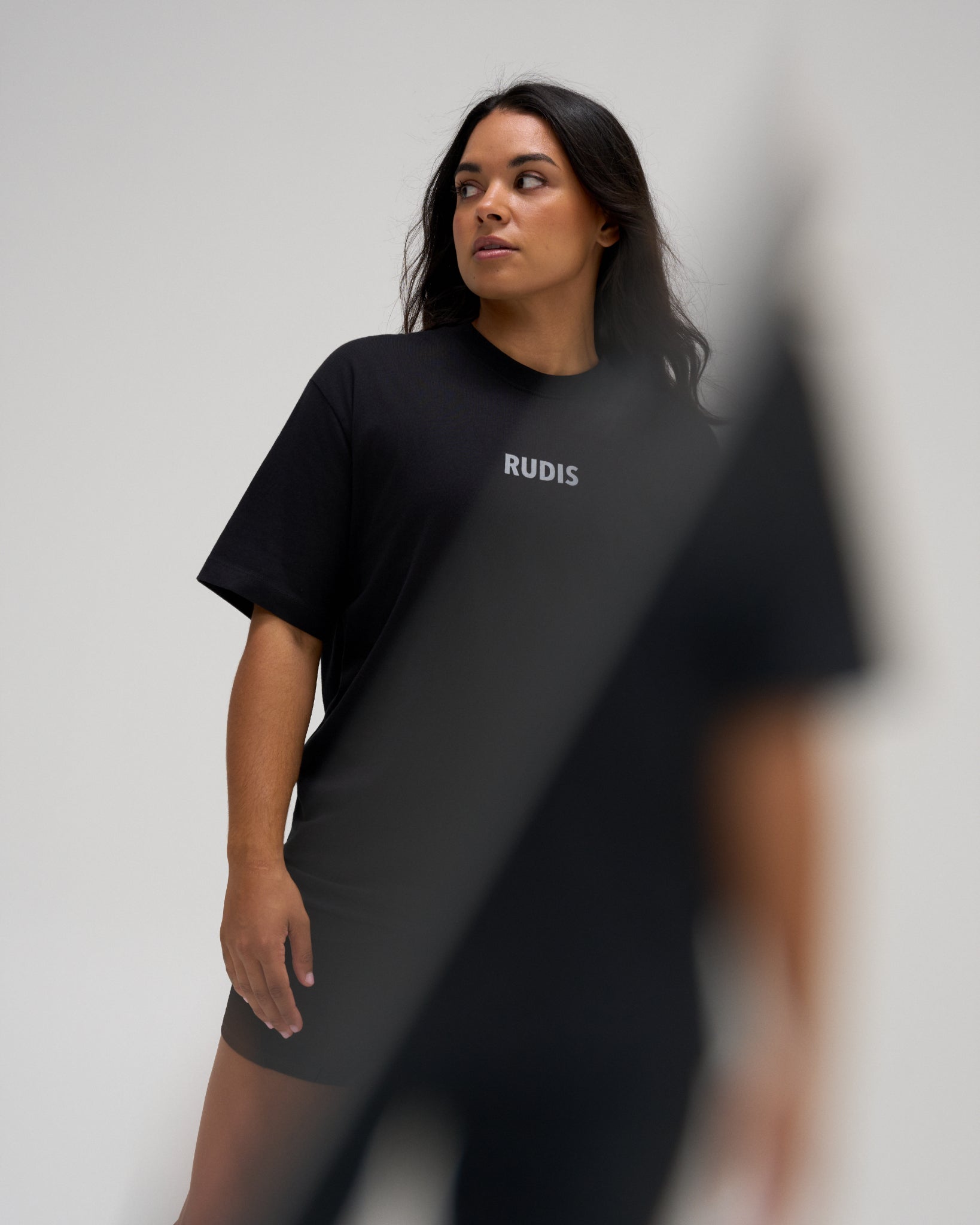 Female model wearing the RUDIS Wrestling Back Relaxed Cotton T-Shirt in Black with a centered RUDIS chest logo, short sleeves, and a relaxed silhouette.