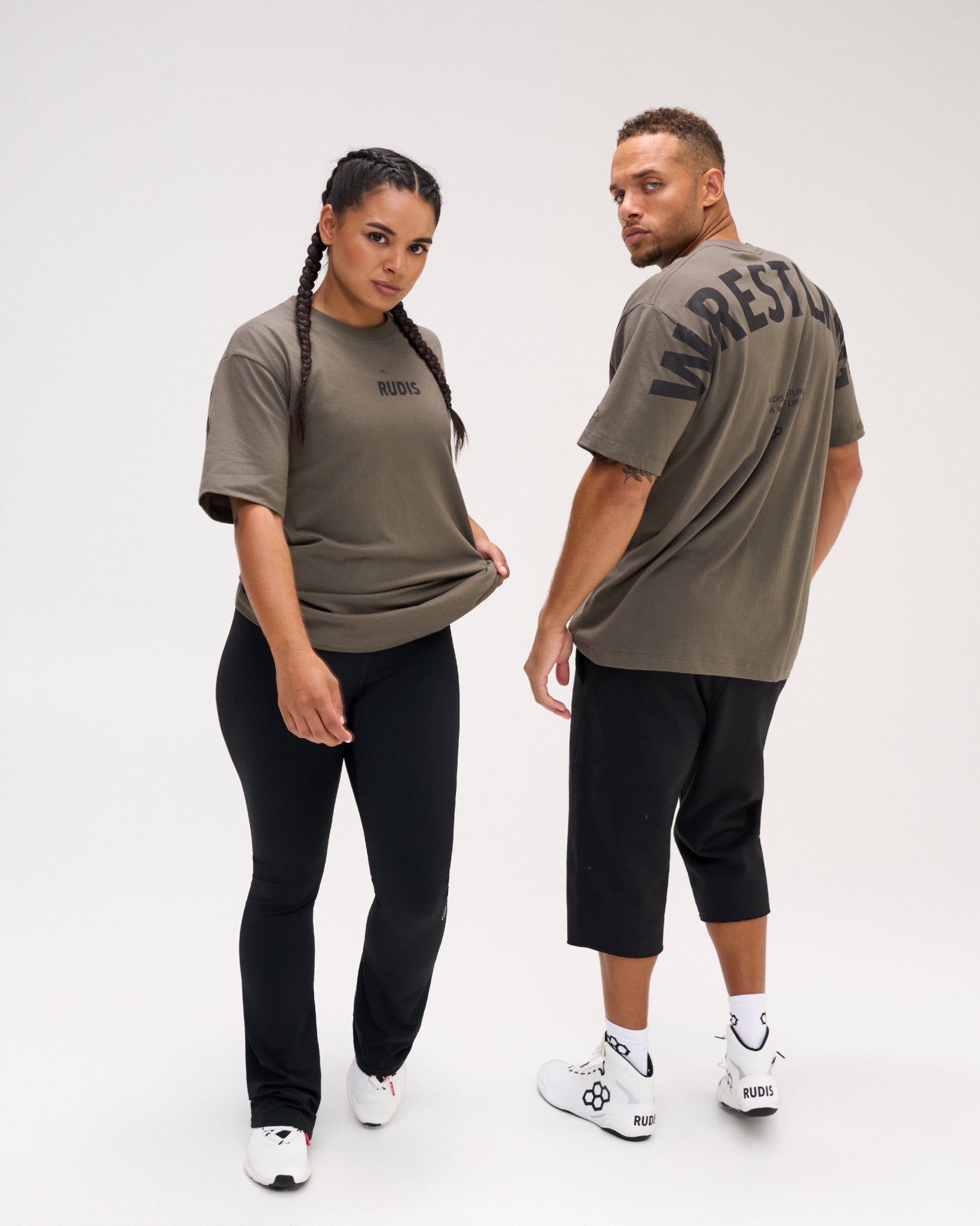 Male and female models wearing the RUDIS Wrestling Back Relaxed Cotton T-Shirt in Dark Olive, displaying the black RUDIS chest logo and bold WRESTLING back lettering.