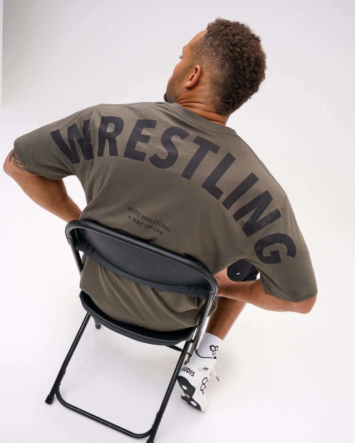 Close-up back view of the RUDIS Wrestling Back Relaxed Cotton T-Shirt in Dark Olive, featuring oversized black WRESTLING lettering and RUDIS Wrestling A Way of Life text.