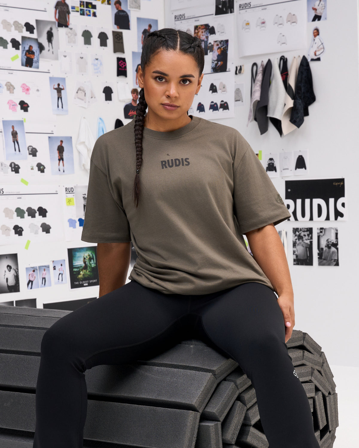 Female model wearing the RUDIS Wrestling Back Relaxed Cotton T-Shirt in Dark Olive, showing the minimal black RUDIS chest logo and relaxed short-sleeve fit.