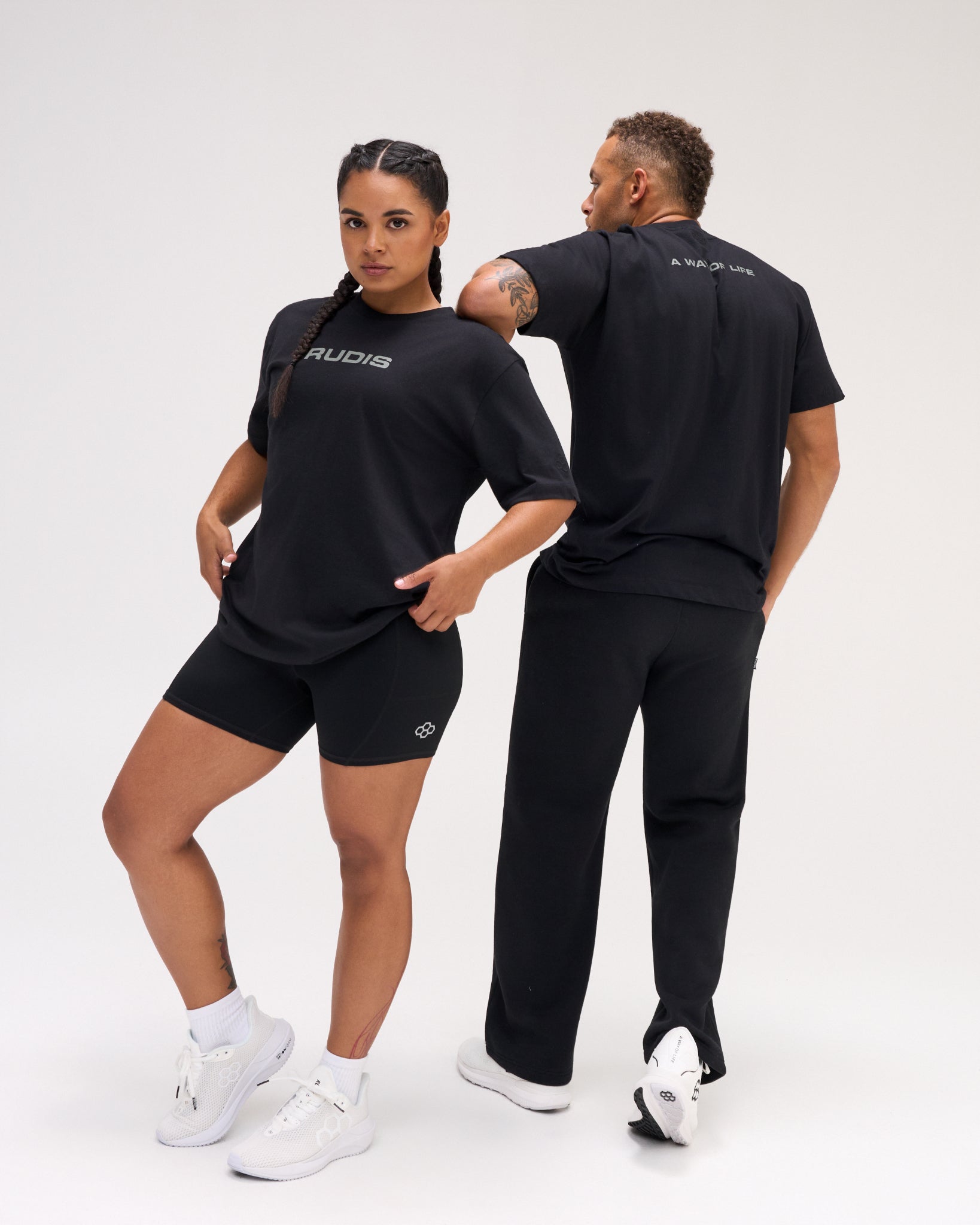 Two models wearing black RUDIS relaxed cotton T-shirts, showing the front logo and large WRESTLING back graphic.