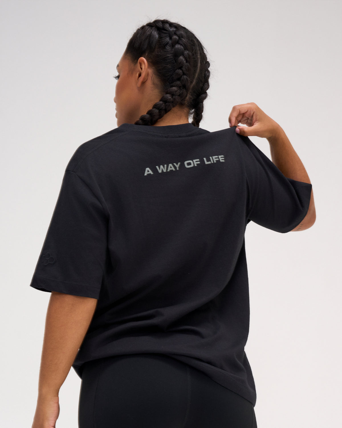 Back view of female model wearing the black RUDIS Relaxed Cotton T-Shirt featuring gray A WAY OF LIFE lettering across the upper back.