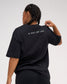 Back view of female model wearing the black RUDIS Relaxed Cotton T-Shirt featuring gray A WAY OF LIFE lettering across the upper back.