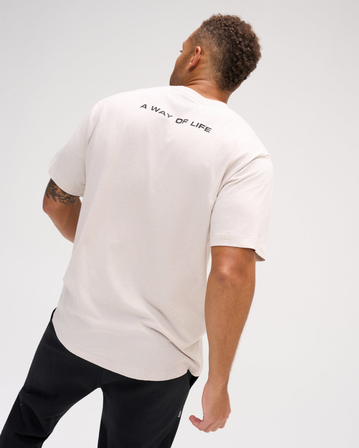 Back view of male model wearing the bone RUDIS Relaxed Cotton T-Shirt with A WAY OF LIFE lettering printed across the upper back.