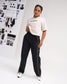 Female model wearing a bone RUDIS Relaxed Cotton T-Shirt with black RUDIS chest logo, paired with black athletic pants featuring white piping.