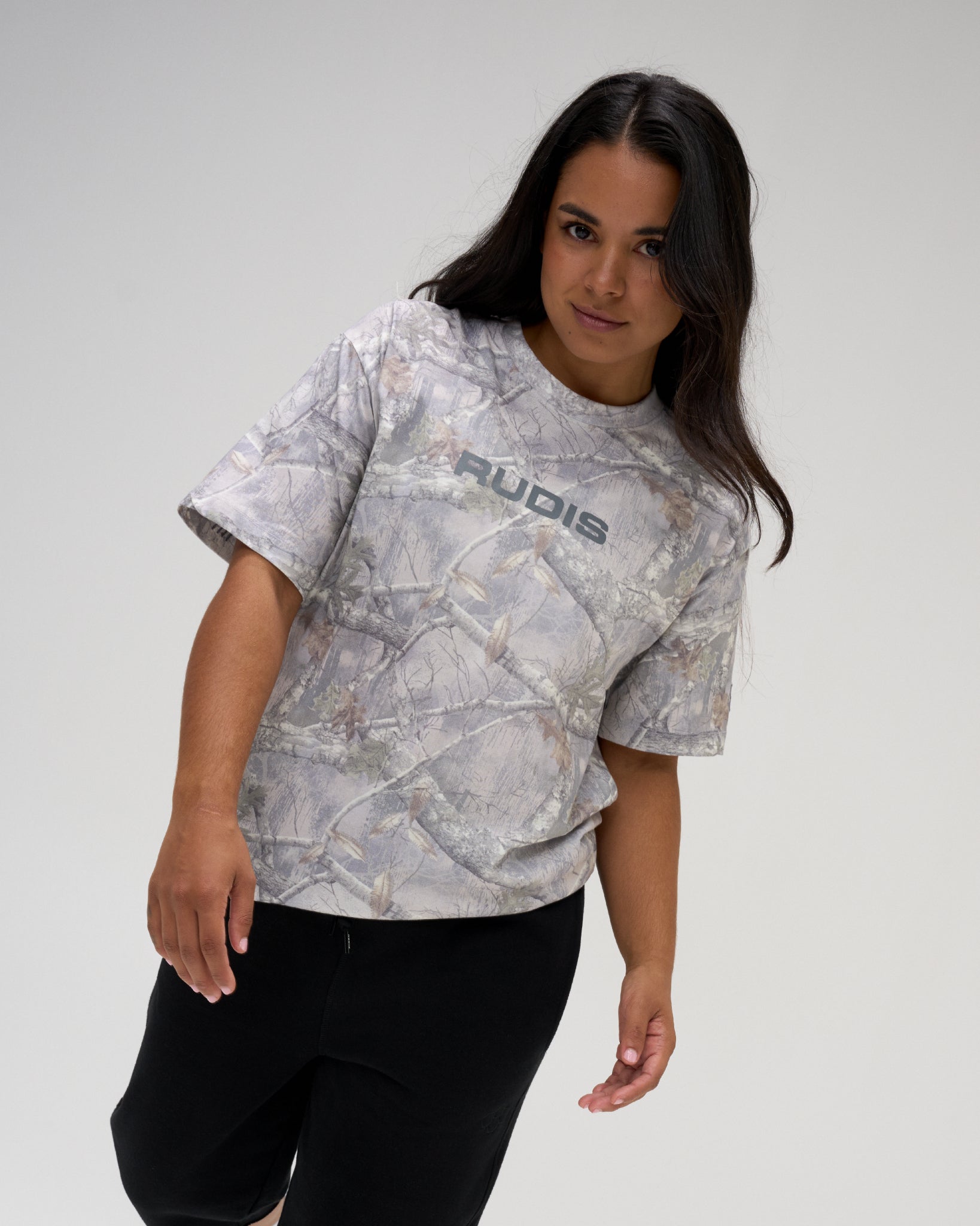 Female model wearing the RUDIS Relaxed Cotton T-Shirt in light gray tree camo with a gray RUDIS chest logo and black athletic pants.