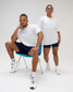 Male and female models wearing white RUDIS Relaxed Cotton T-Shirts with light blue RUDIS chest logos, paired with navy athletic bottoms.