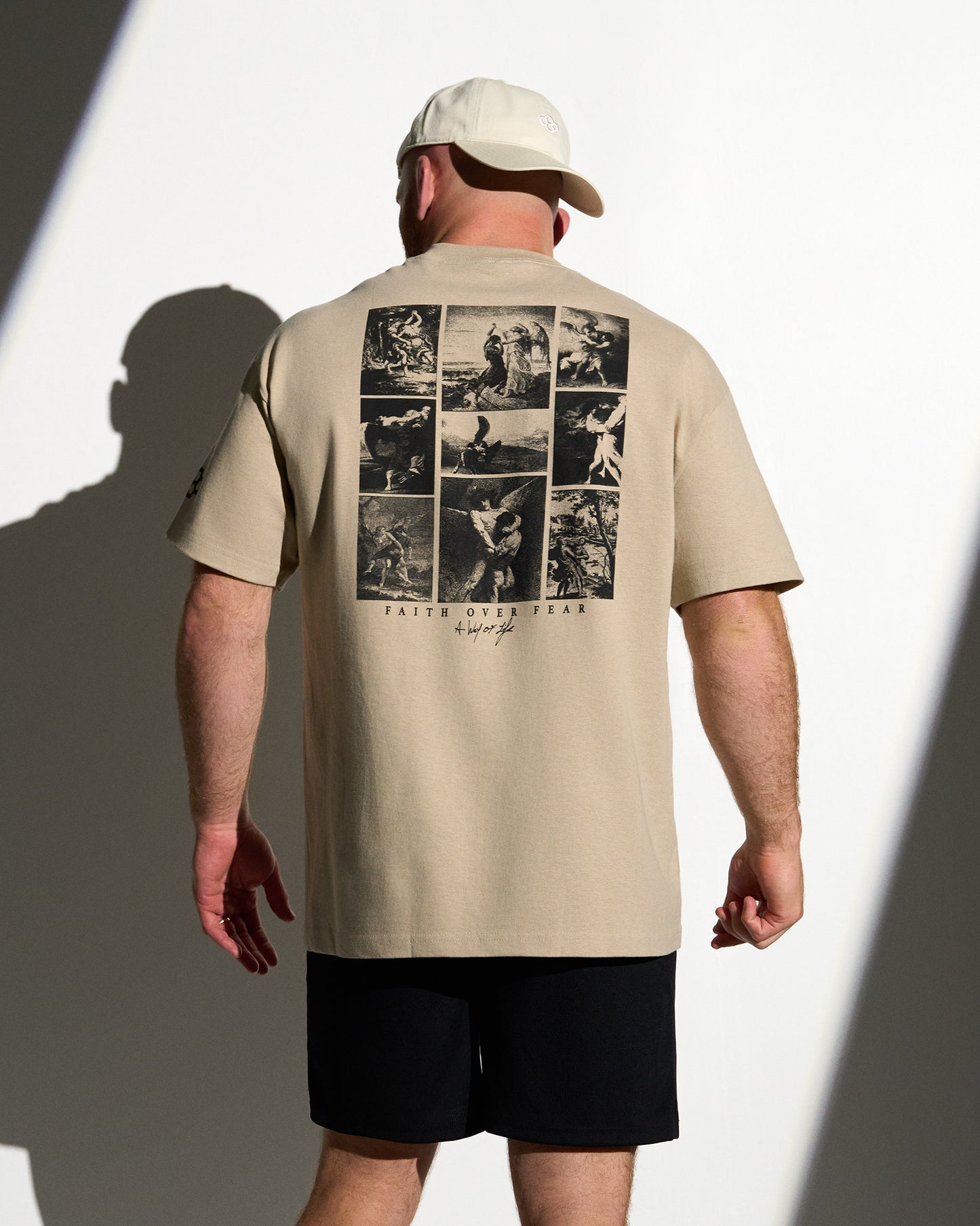 Man wearing a beige t-shirt with graphic design on the back, standing against a white background.