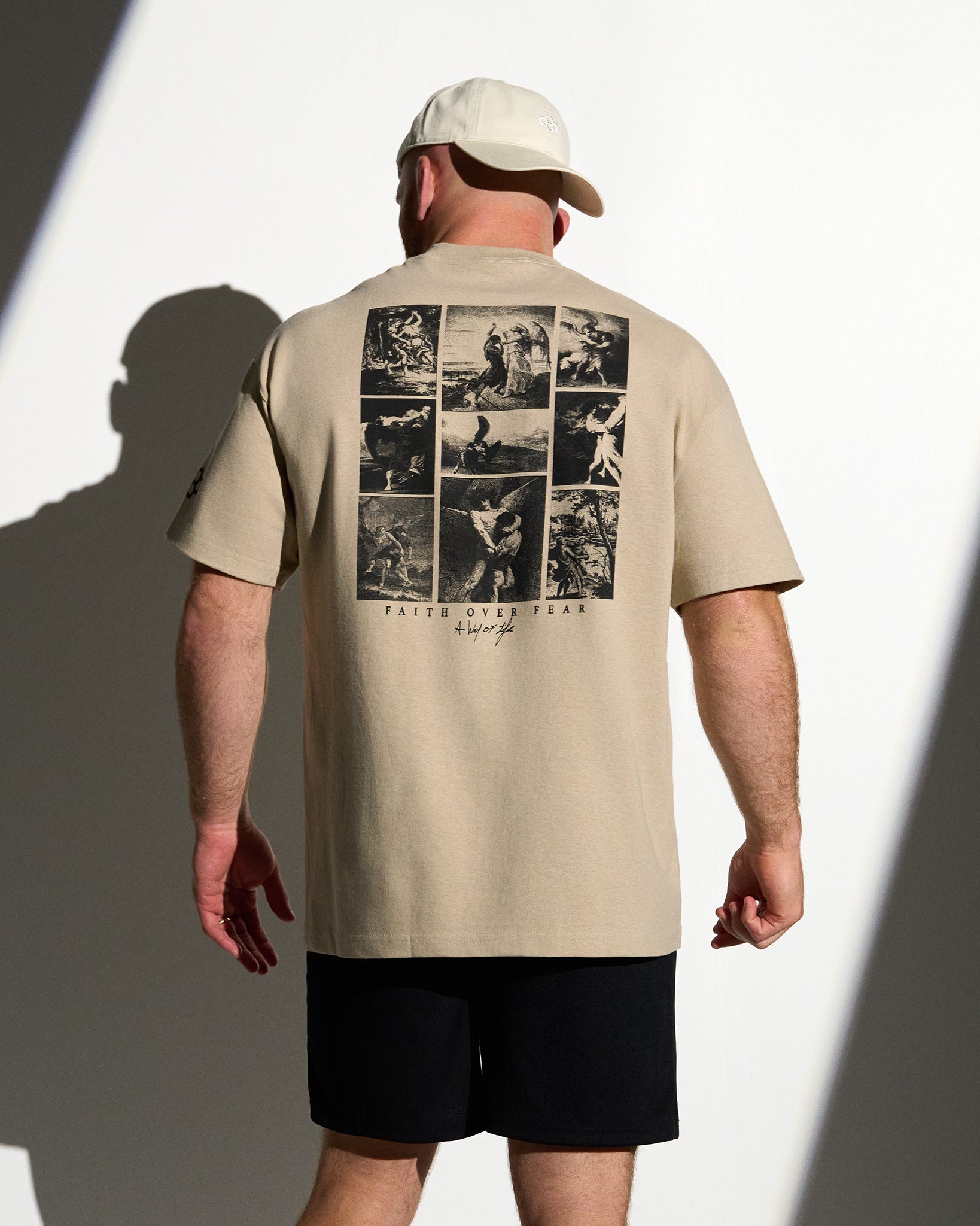 Man wearing a beige t-shirt with graphic design on the back, standing against a white background.
