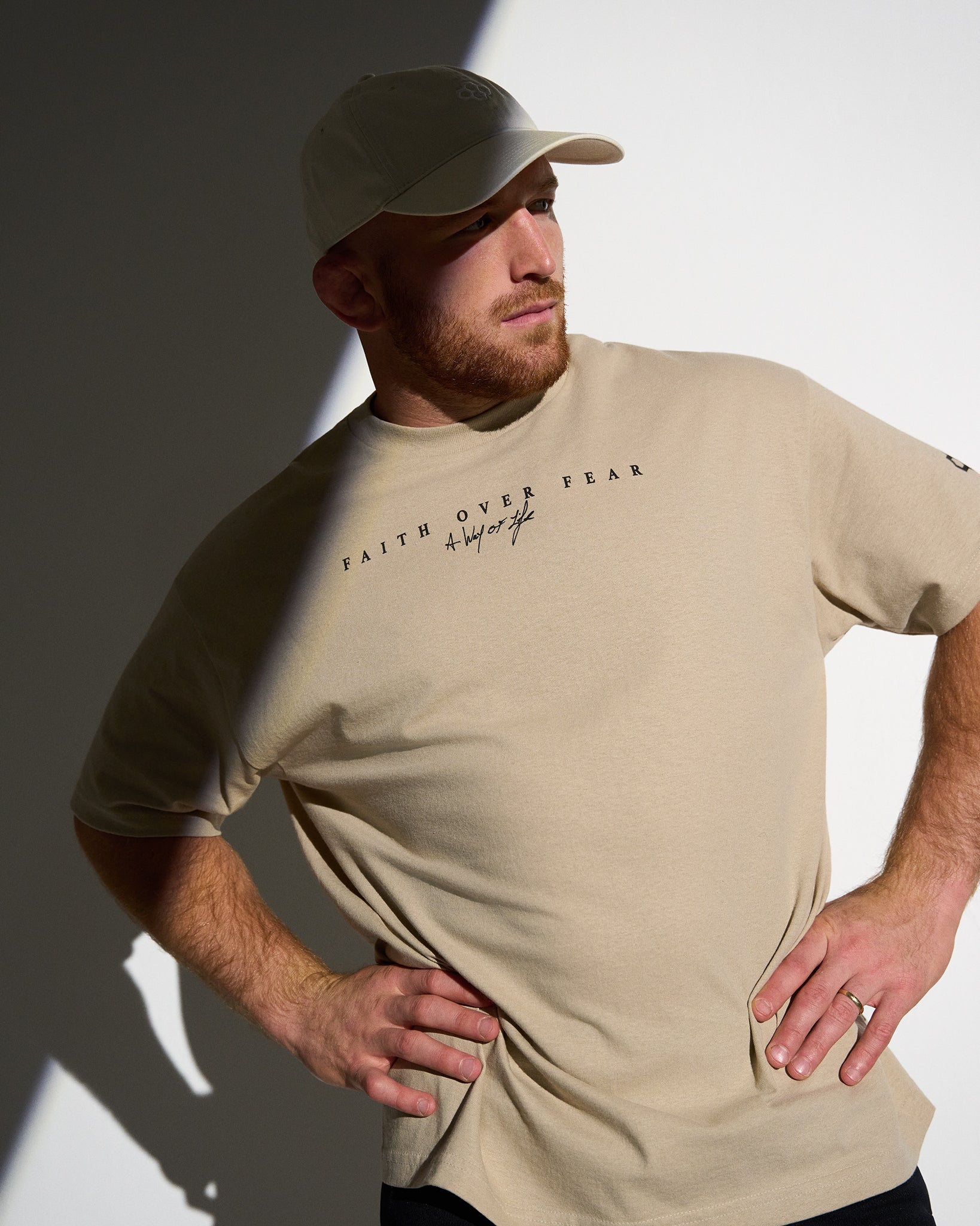 Man wearing a beige t-shirt with text, standing against a white background