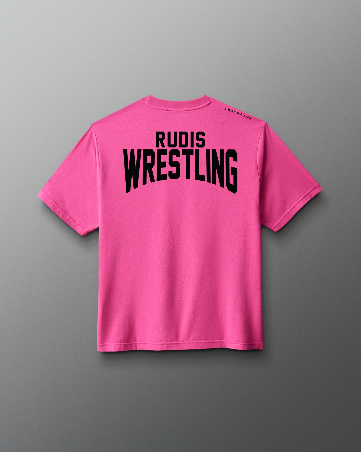 A bright pink short-sleeve t-shirt shown from the back, featuring the words 'RUDIS WRESTLING' printed in bold black capital letters across the upper back, set against a dark gray gradient background.