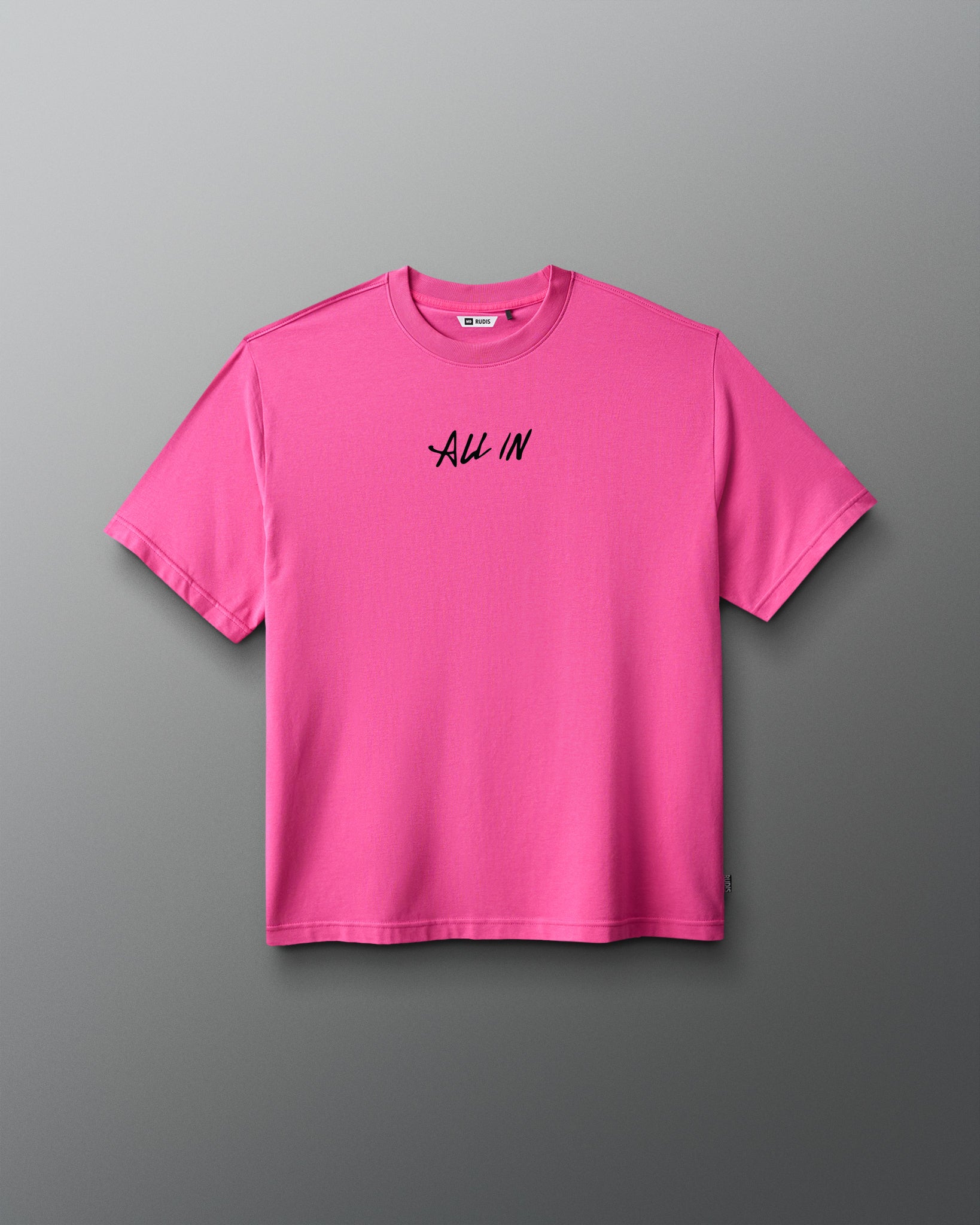 A bright pink short-sleeve crewneck t-shirt with the words 'ALL IN' printed in black script across the chest, displayed against a dark gray gradient background.