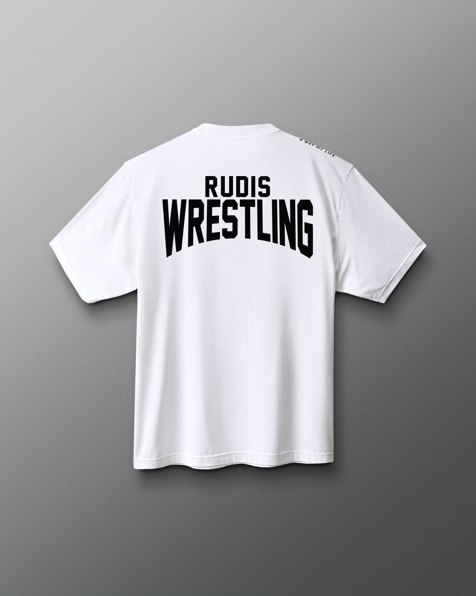 A white short-sleeve t-shirt shown from the back, featuring the words 'RUDIS WRESTLING' printed in bold black letters across the upper back, set against a dark gray gradient background.