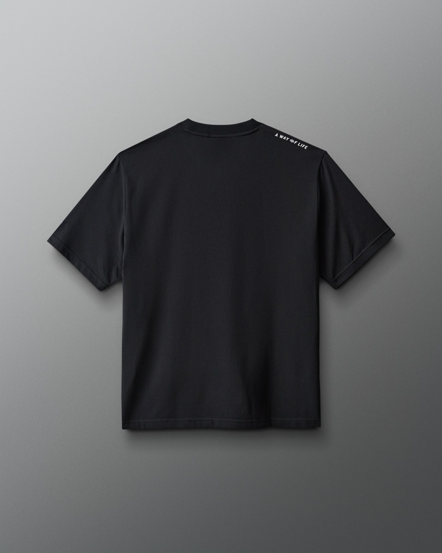 A black short-sleeve t-shirt shown from the back, featuring a small white text print on the left shoulder, displayed against a neutral gray background.