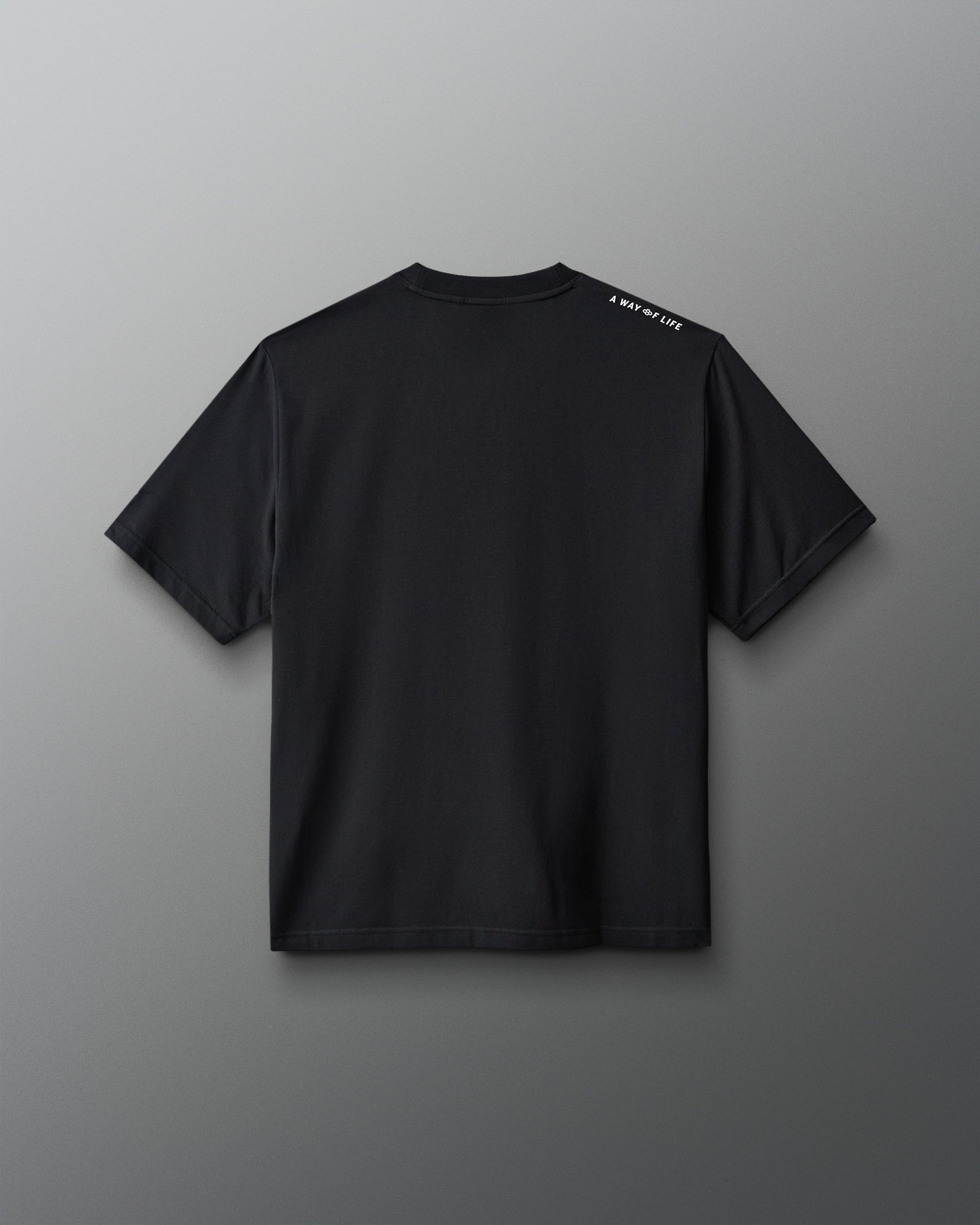A black short-sleeve t-shirt shown from the back, featuring a small white text print on the left shoulder, displayed against a neutral gray background.