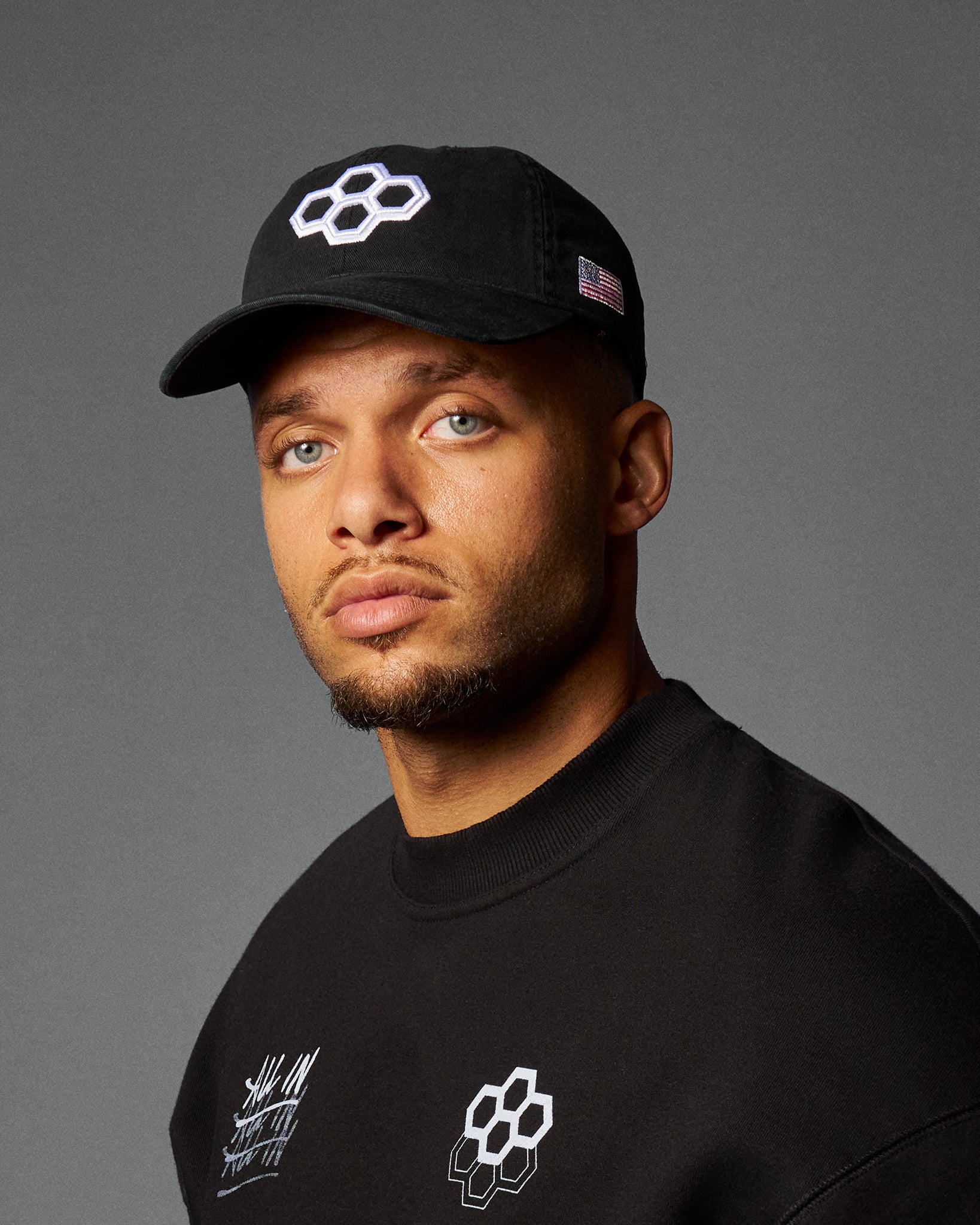 Man wearing a black cap and black shirt with logos on a gray background