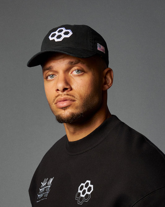 Man wearing a black cap and black shirt with logos on a gray background