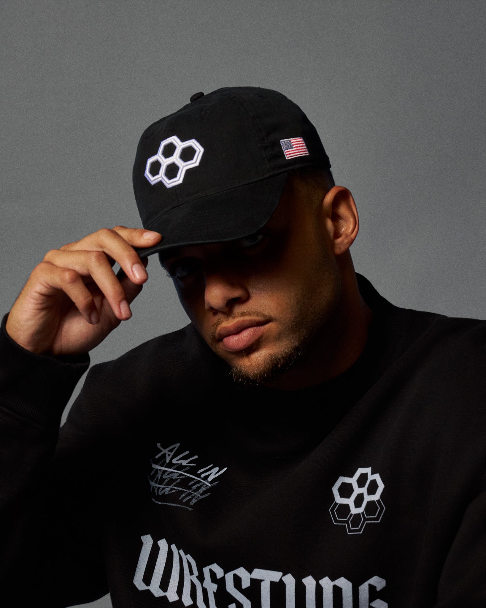 Person wearing a black cap and sweatshirt with logos on a gray background