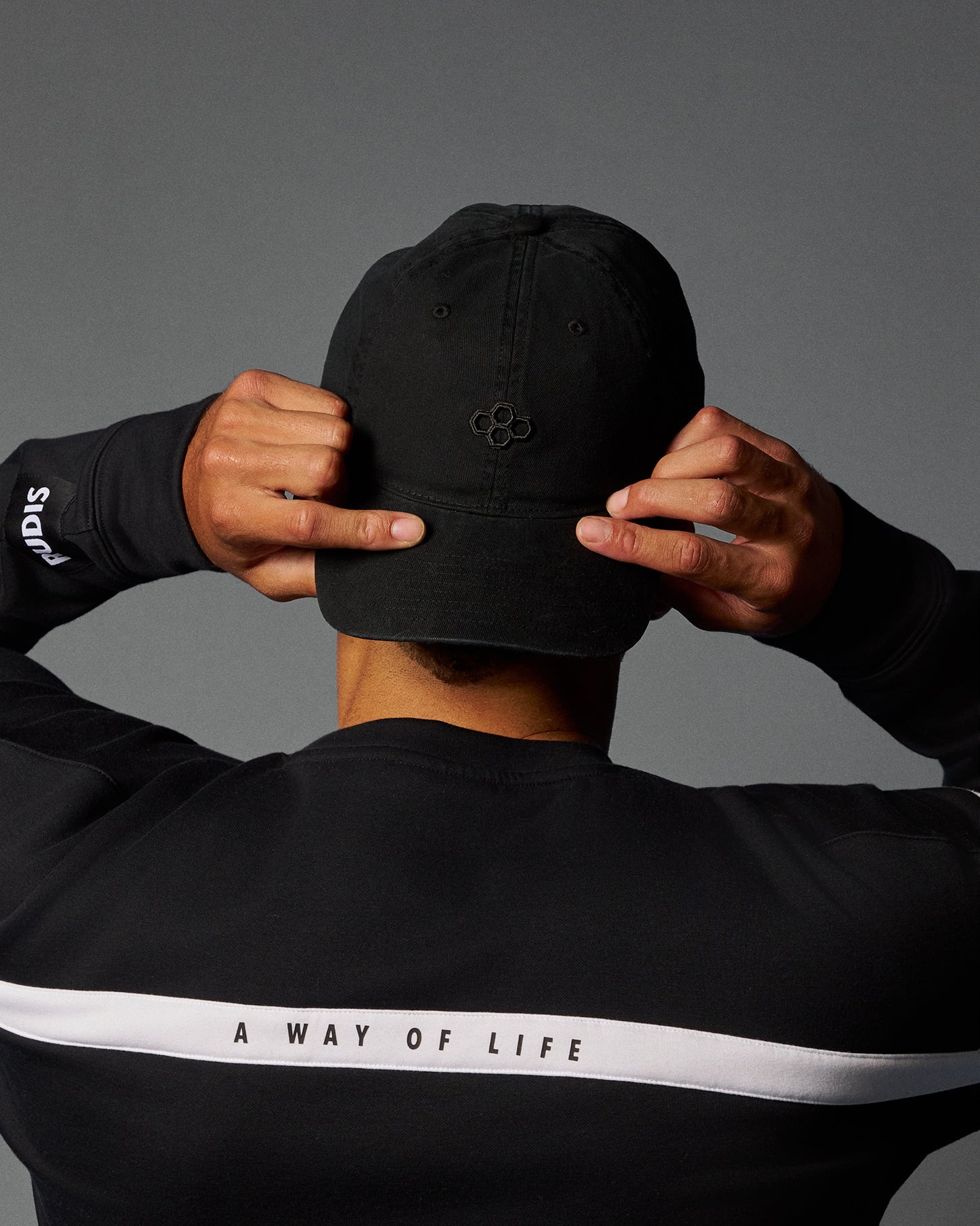 Person wearing a black cap and black jacket with 'A Way of Life' text on a gray background