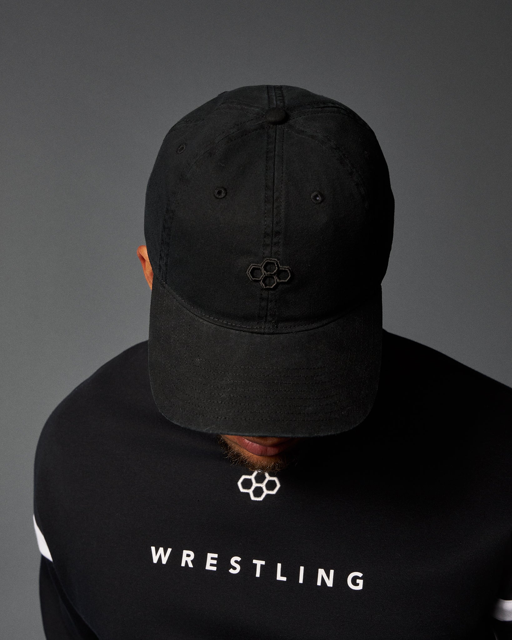Person wearing a black cap and black 'Wrestling' shirt on a gray background
