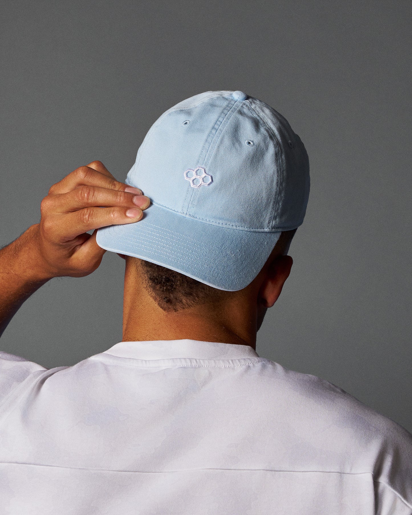 Person wearing a light blue cap with a logo on a gray background