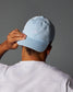 Person wearing a light blue cap with a logo on a gray background