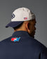Person wearing a cap with an American flag and a jacket with a map design on the back against a gray background