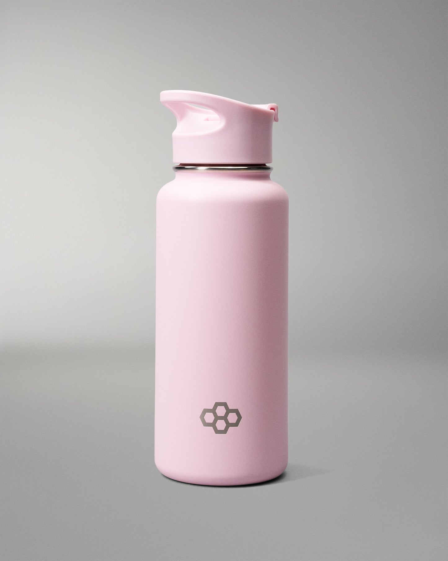 A matte light pink insulated water bottle with a matching pink flip-top lid, featuring a small dark gray geometric logo near the bottom, set against a neutral gray studio background.