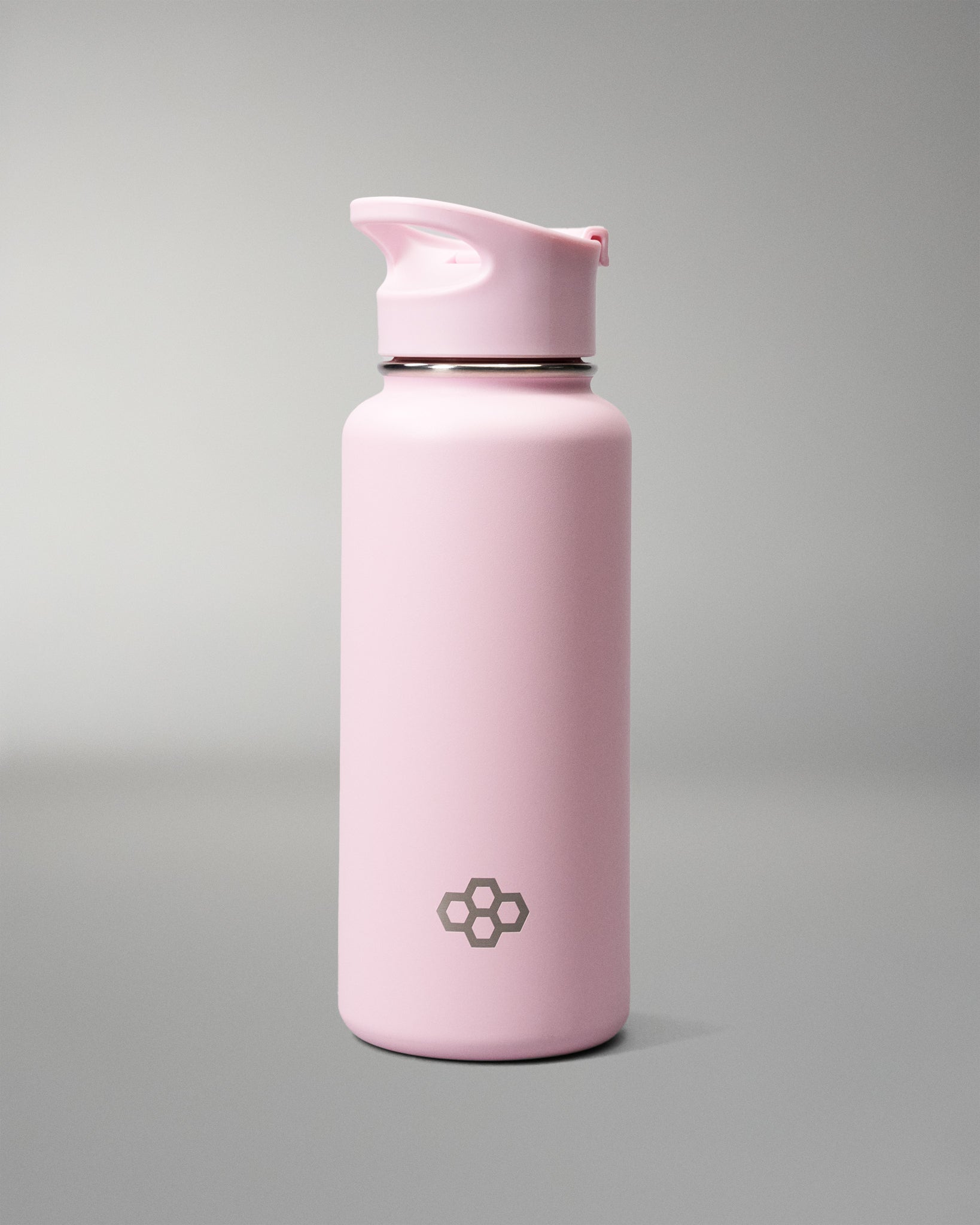 A matte light pink insulated water bottle with a matching pink flip-top lid, featuring a small dark gray geometric logo near the bottom, set against a neutral gray studio background.