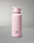 A matte light pink insulated water bottle with a matching pink flip-top lid, featuring a small dark gray geometric logo near the bottom, set against a neutral gray studio background.