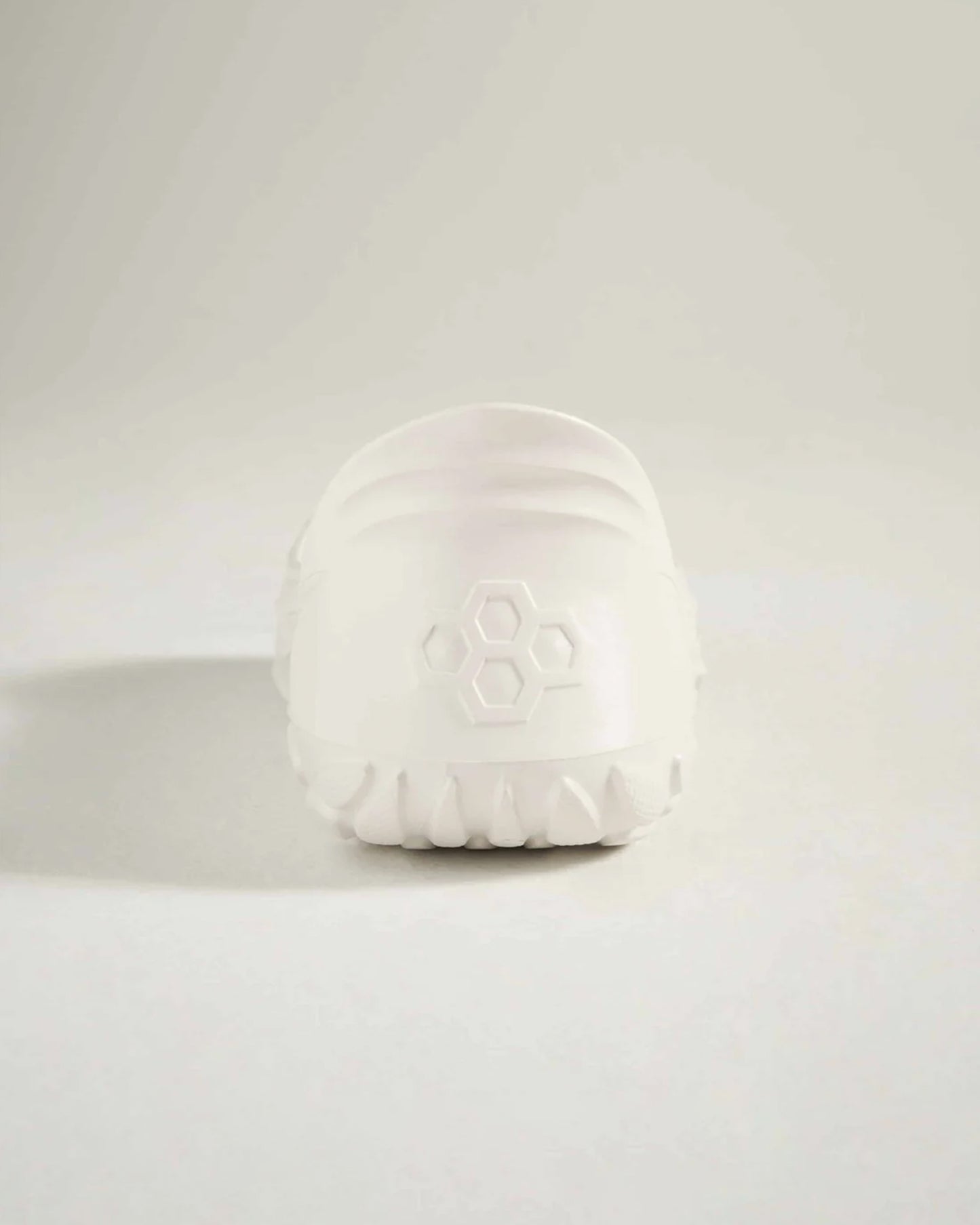 A minimalist white shoe showcasing a smooth rounded silhouette with a textured sole for traction